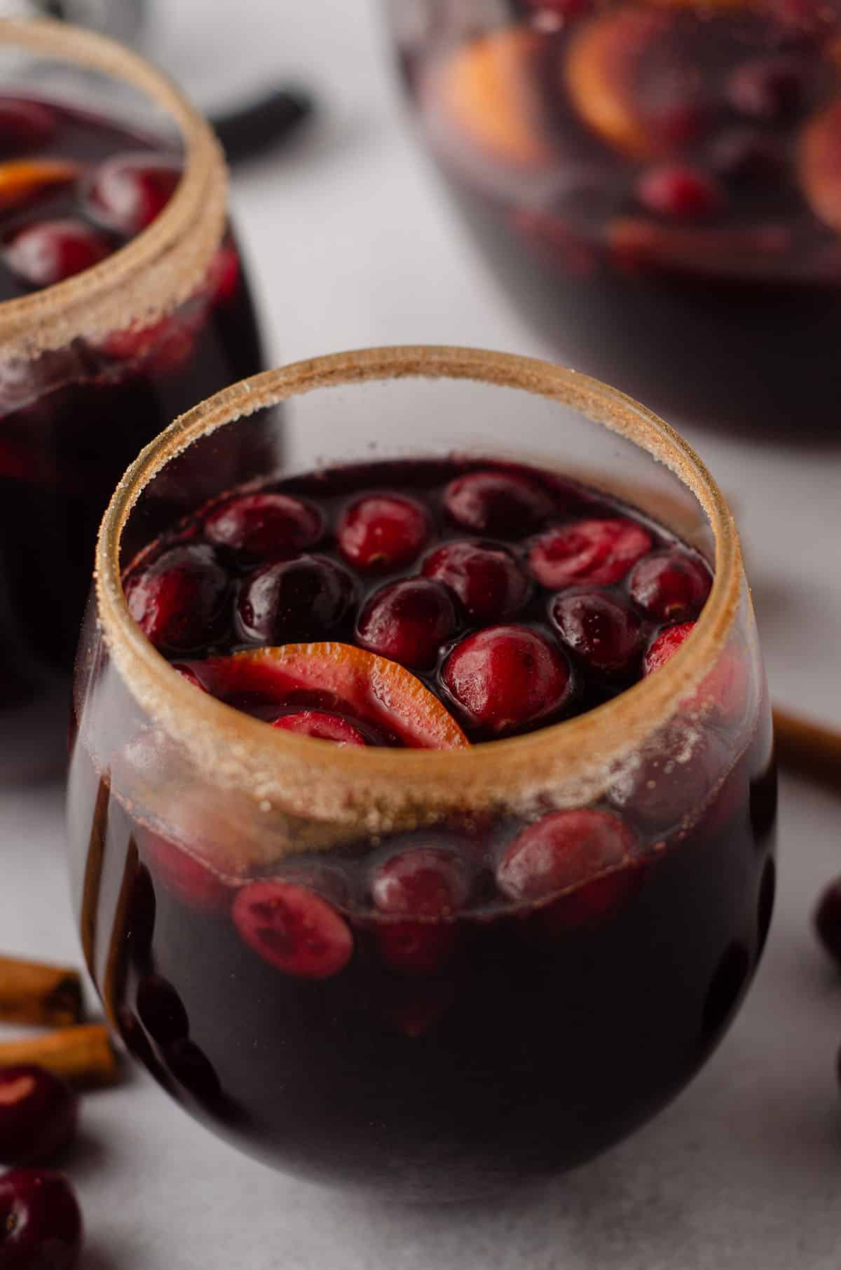 cranberry and orange winter sangria sitting in a glass with a cinnamon sugared rim