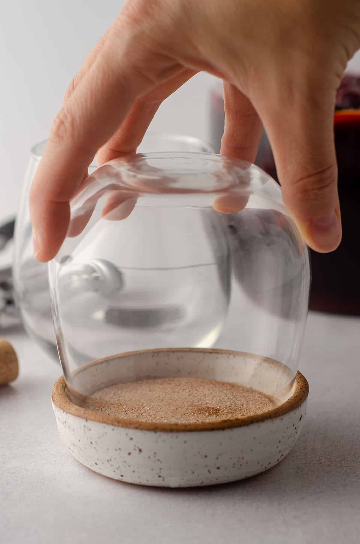 hand dipping a wine glass into a bowl of cinnamon sugar to make a cinnamon sugared rim for sangria