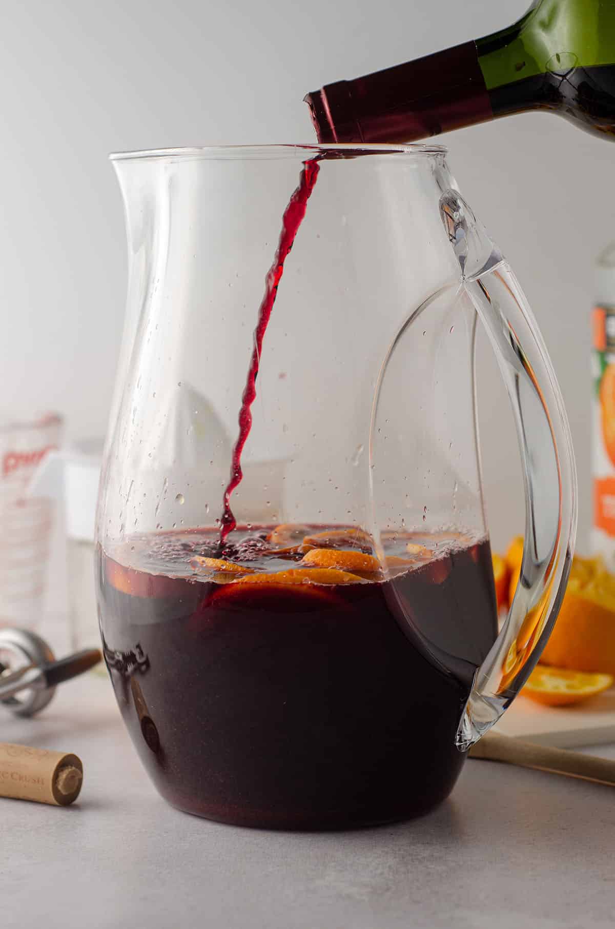 pouring red wine into a pitcher of oranges for sangria