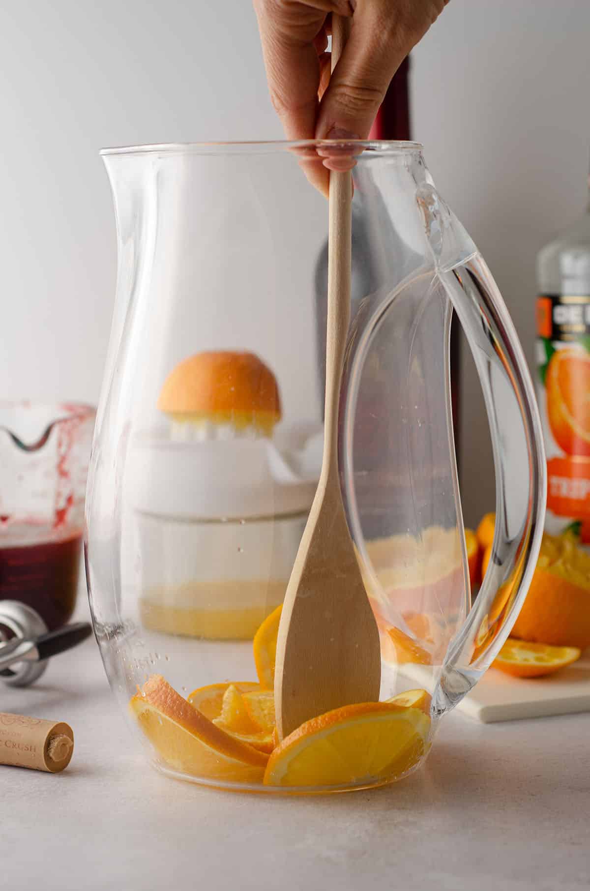 muddling oranges in a pitcher with a wooden spoon