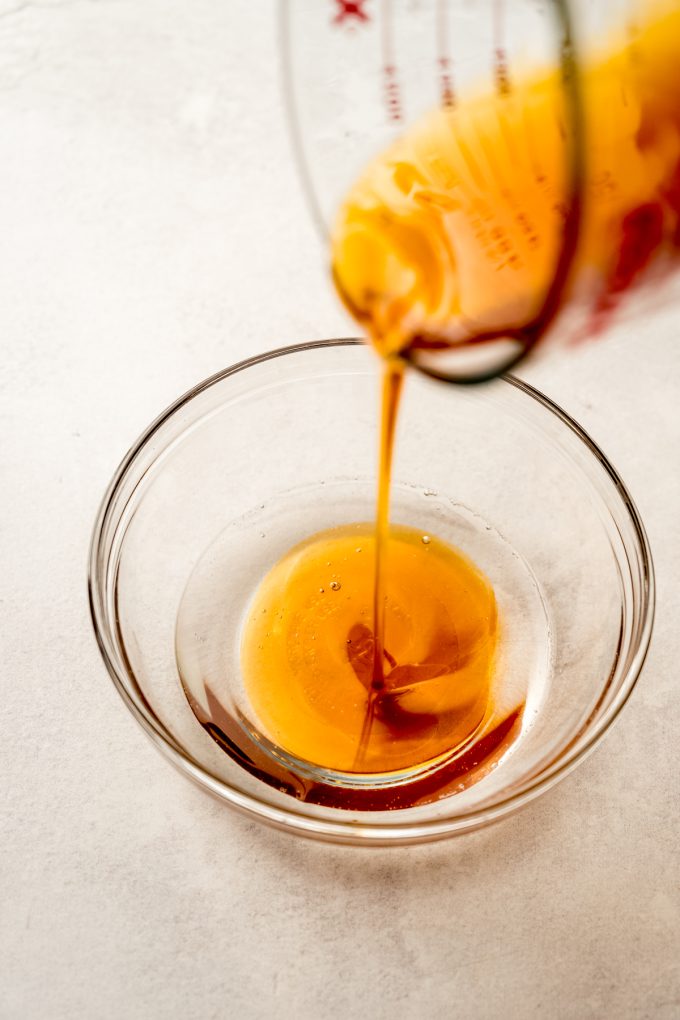 Someone is pouring honey into a bowl of melted coconut oil.