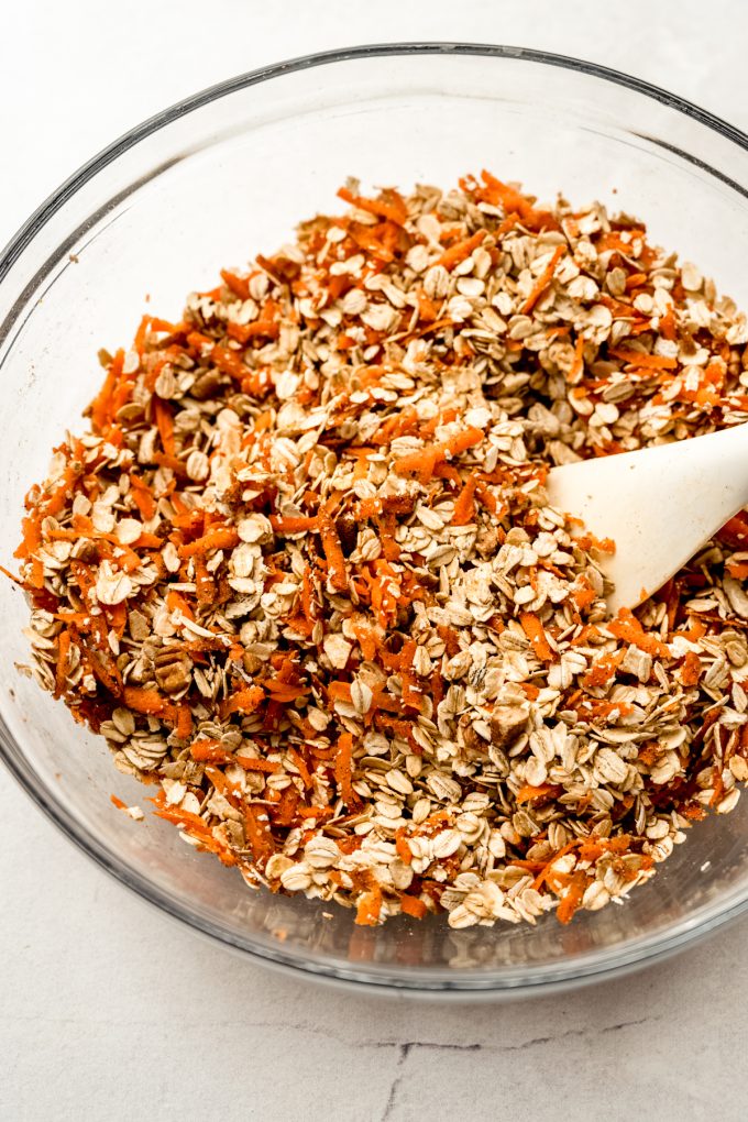 A bowl of ingredients to make carrot cake granola with a spatula in it.