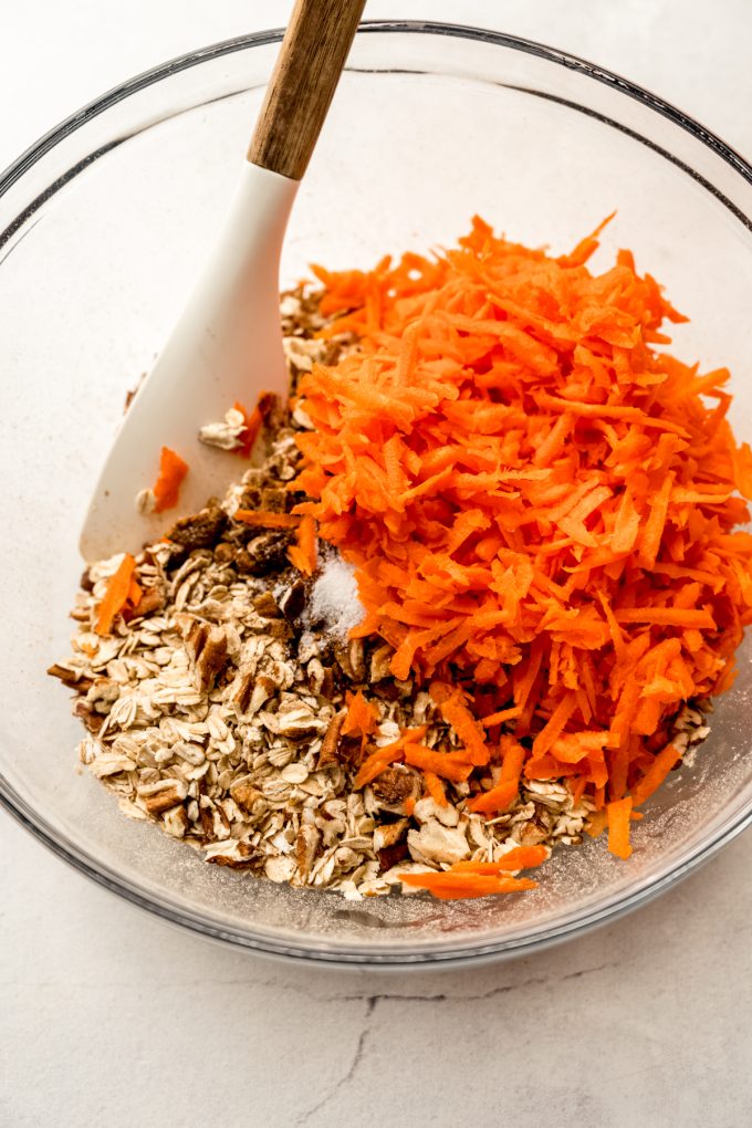 A bowl of ingredients to make carrot cake granola with a spatula in it.