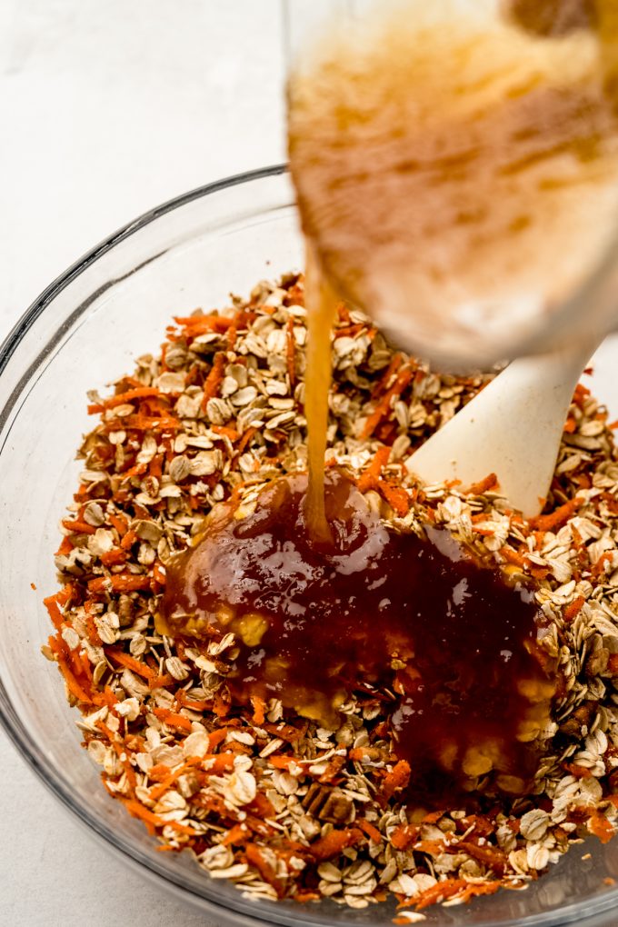 Someone is pouring a mixture of honey and coconut oil over a carrot cake granola mixture.
