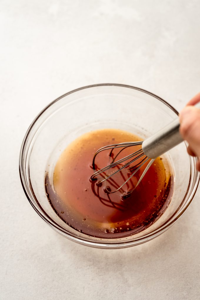 Someone is whisking a bowl of melted coconut oil and honey together.