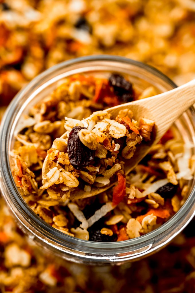 A jar of carrot cake granola with a wooden spoon in it.
