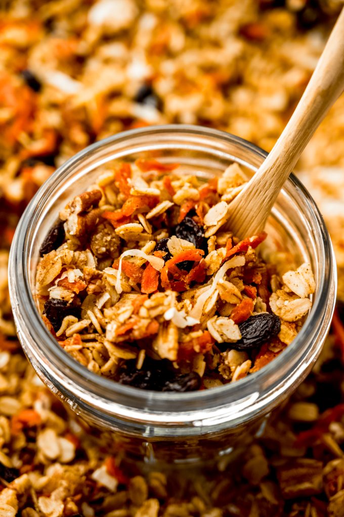 A jar of carrot cake granola with a wooden spoon in it.