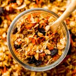 Aerial photo of a jar of carrot cake granola with a wooden spoon in it.