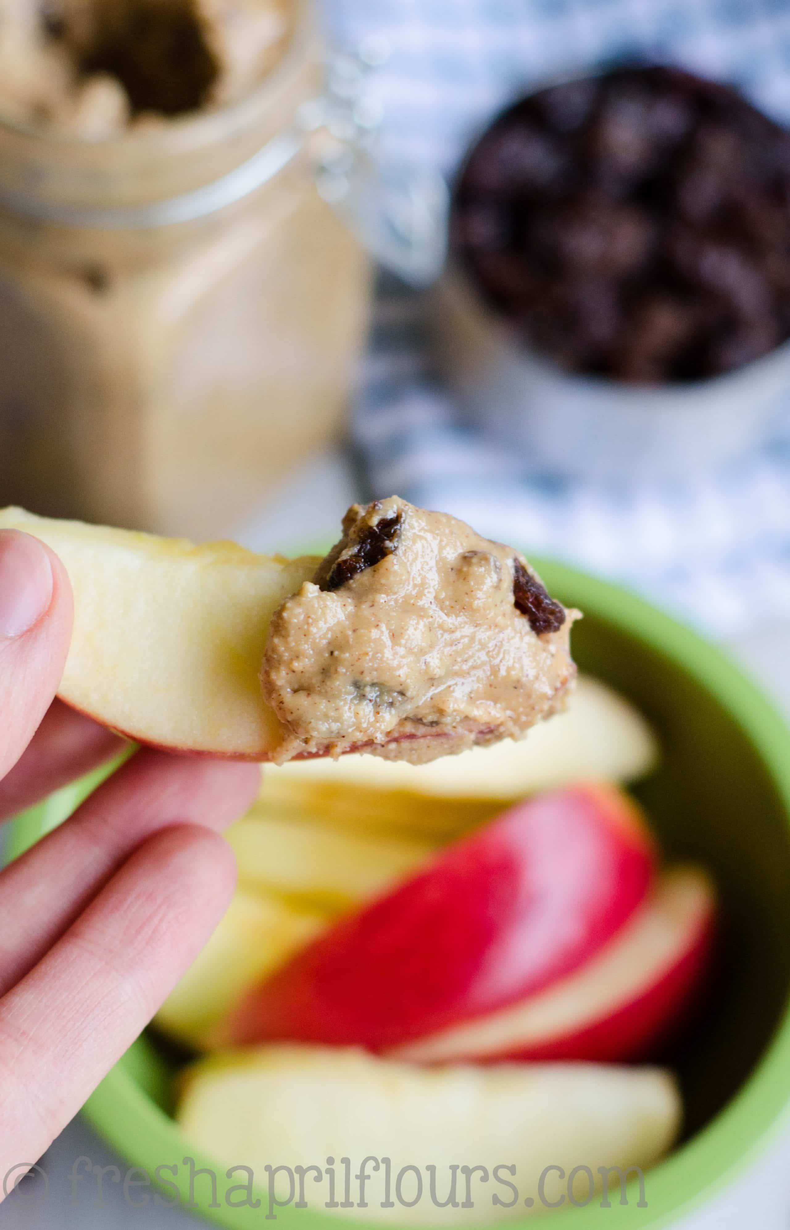 Hand holding an apple slice with cinnamon raisin peanut butter spread on it.