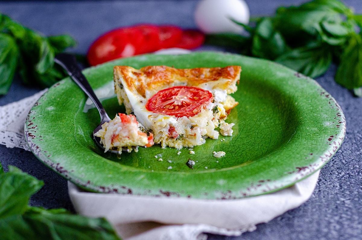 slice of crutless caprese quiche on a green plate with a fork and a bite taken out of it