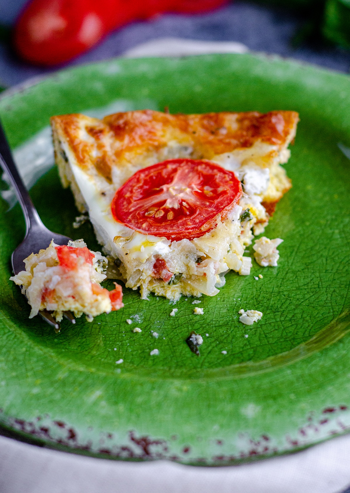 slice of crutless caprese quiche on a green plate with a fork and a bite taken out of it