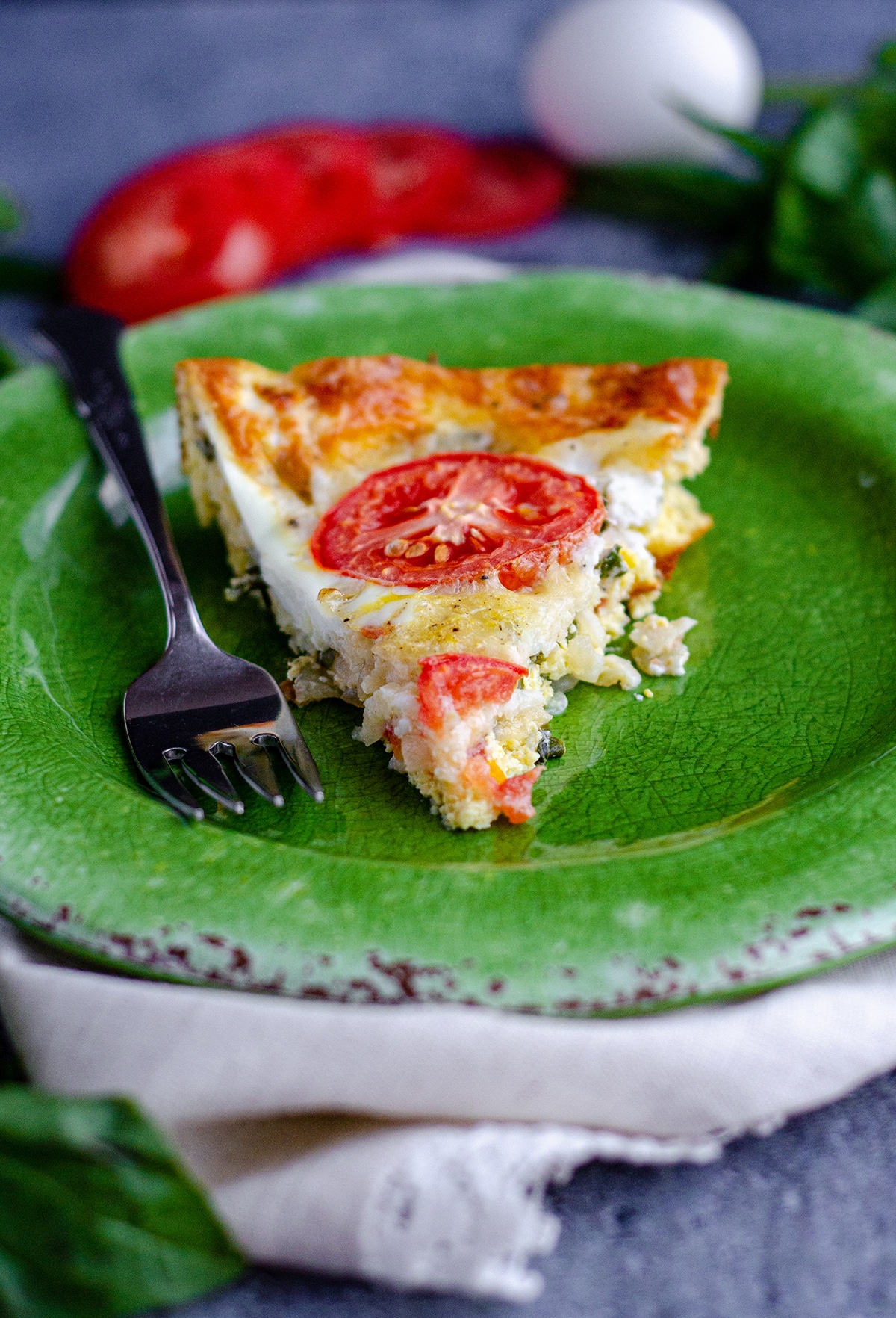 slice of crustless caprese quiche on a green plate with a fork