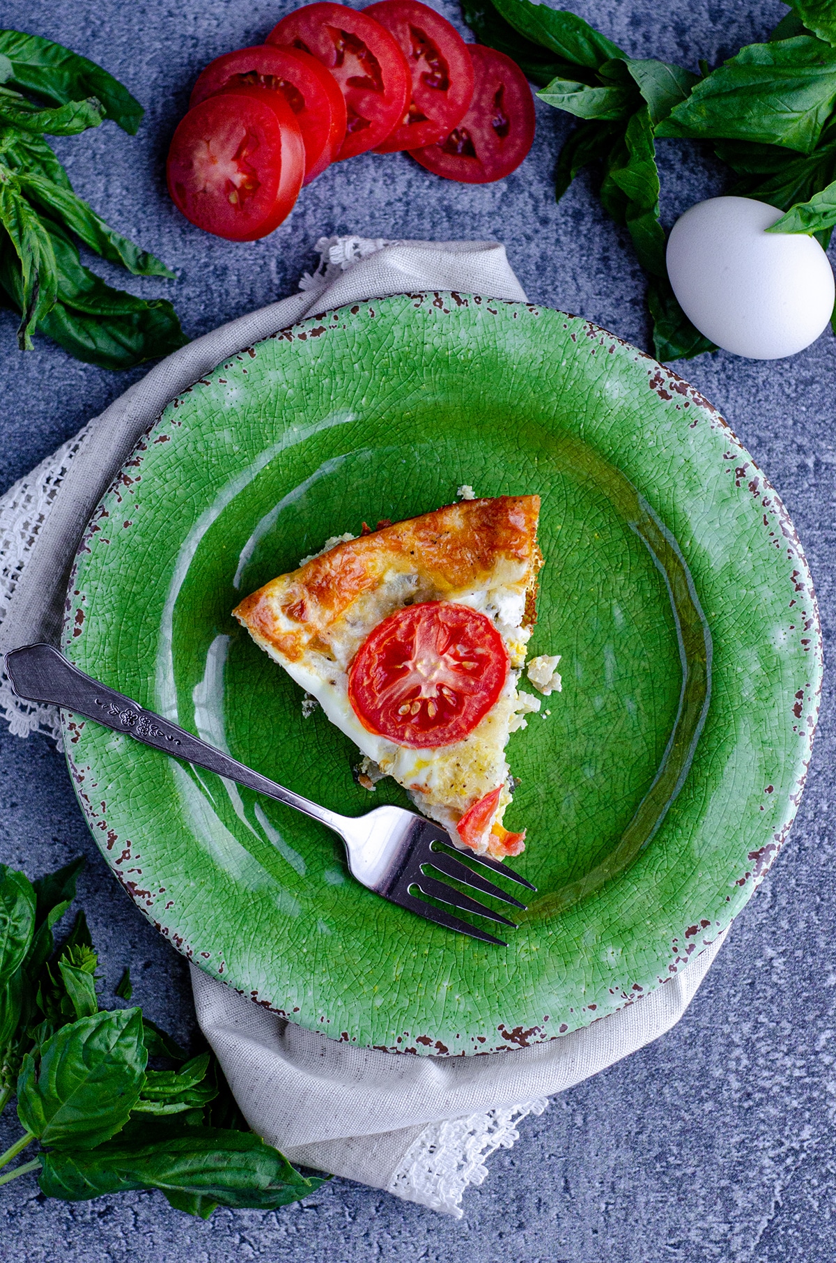 aerial photo of a slice of crustless caprese quiche on a green plate with a fork