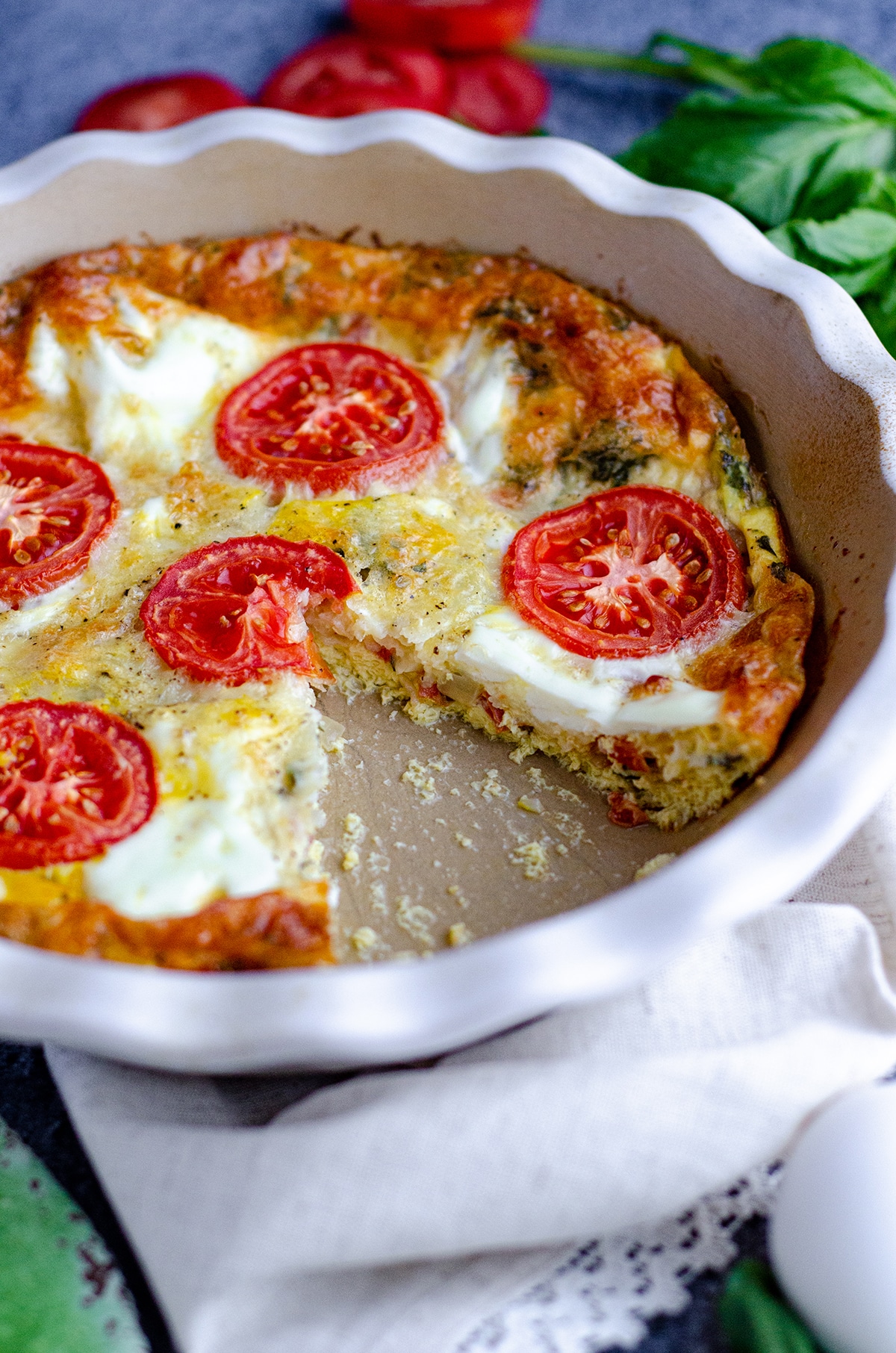 crustless caprese quiche in a pie plate with a slice removed