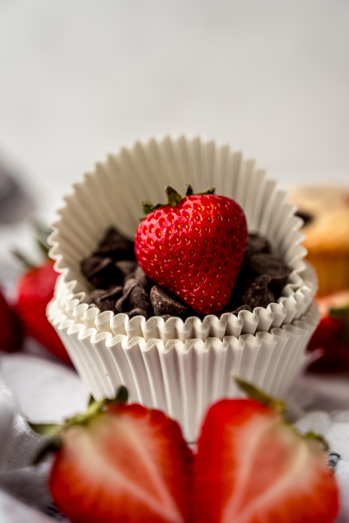 A stack of muffin liners with chocolate chips and a strawberry in it with sliced strawberries in the foreground.