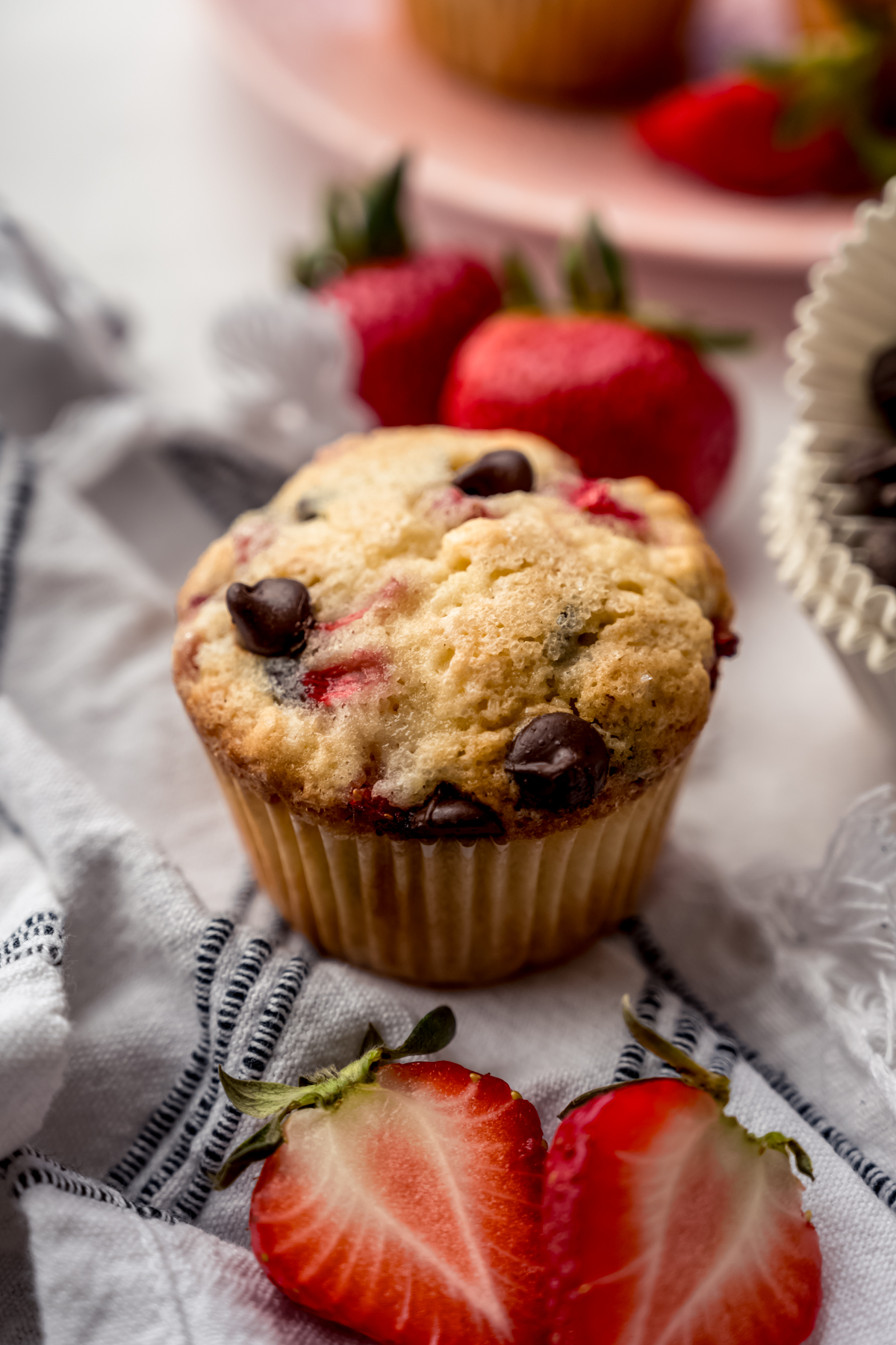 A photo of a strawberry chocolate chip muffin on a kitchen towel with strawberries around it.