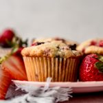 A photo of a strawberry chocolate chip muffin on a plate with strawberries around it.