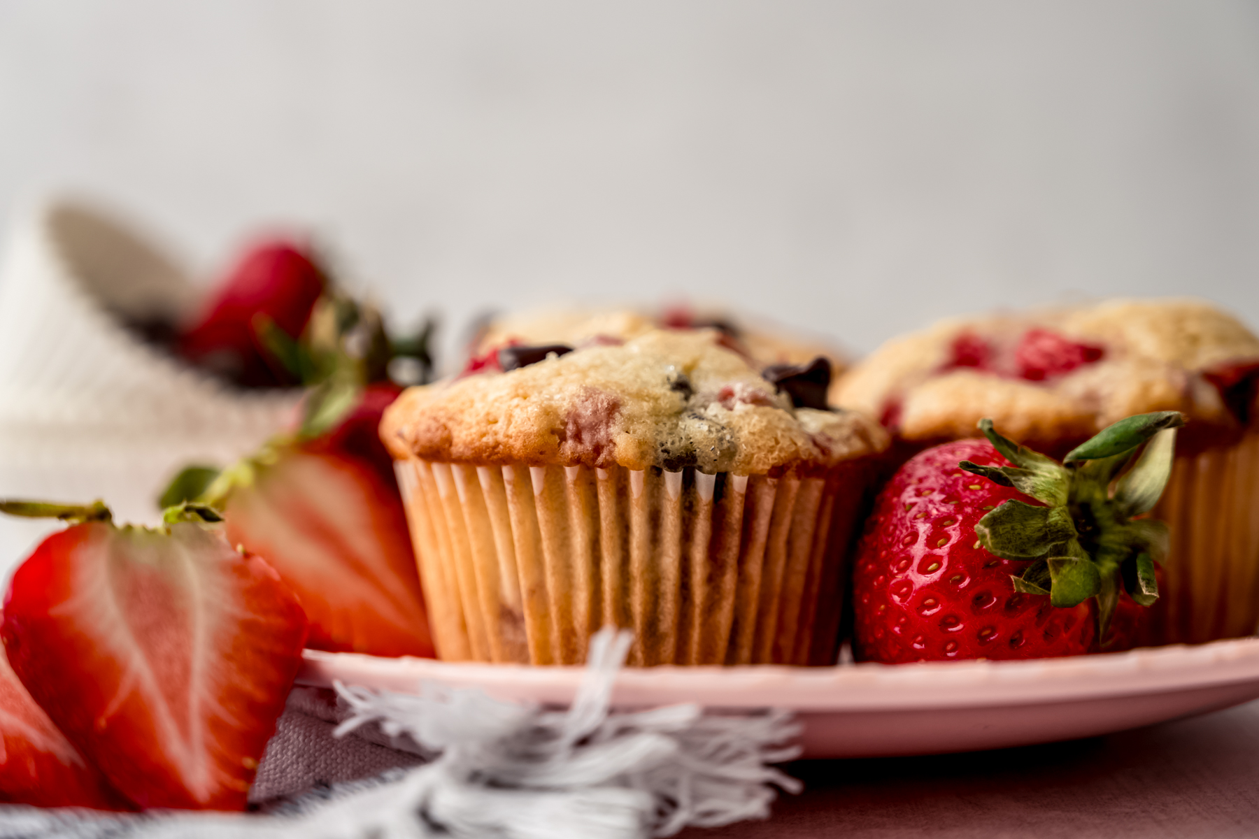 A photo of a strawberry chocolate chip muffin on a plate with strawberries around it.