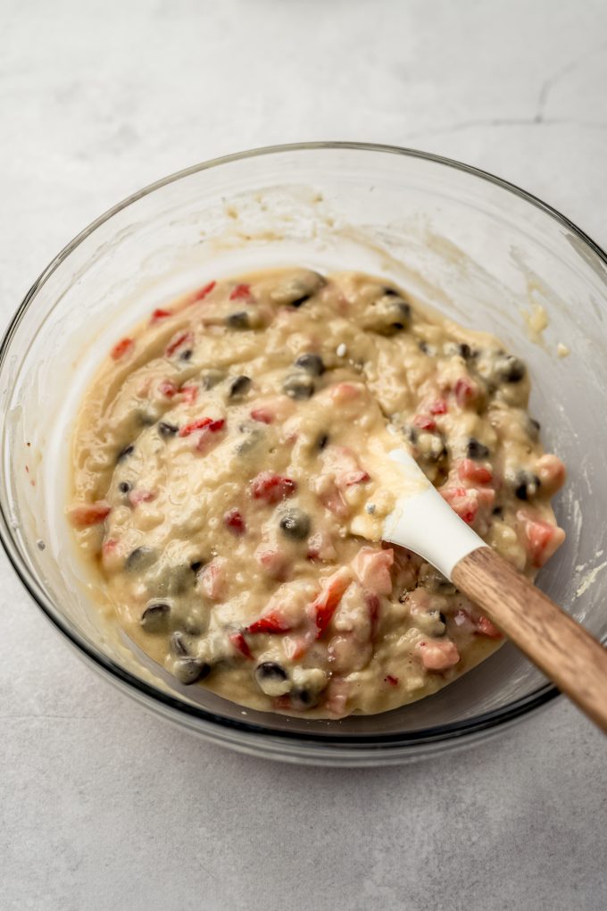 A large glass bowl of strawberry chocolate chip muffin batter with a spatula.