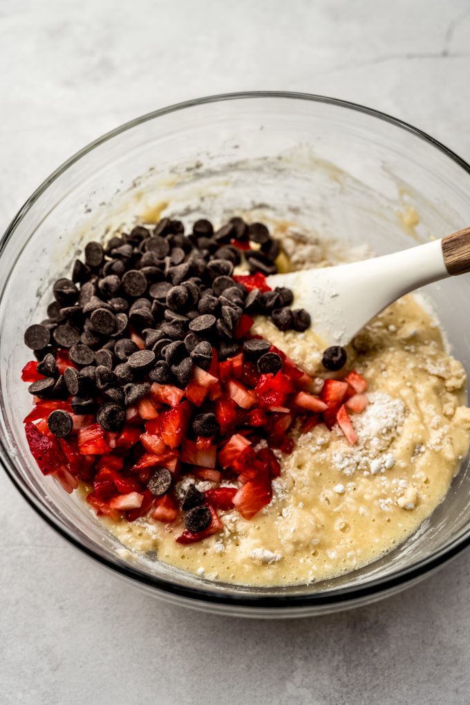 A large glass bowl of strawberry chocolate chip muffin batter before getting stirred together with a spatula.