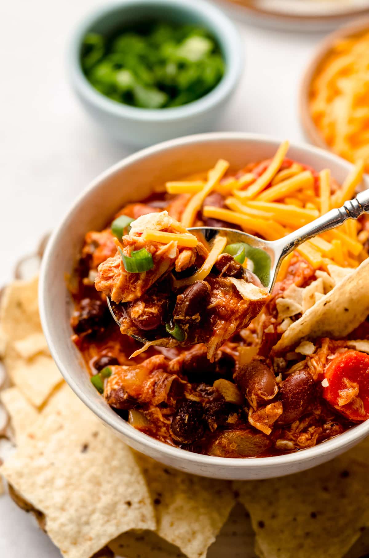 buffalo chicken chili in a bowl on a plate with tortilla chips and a bite on a spoon