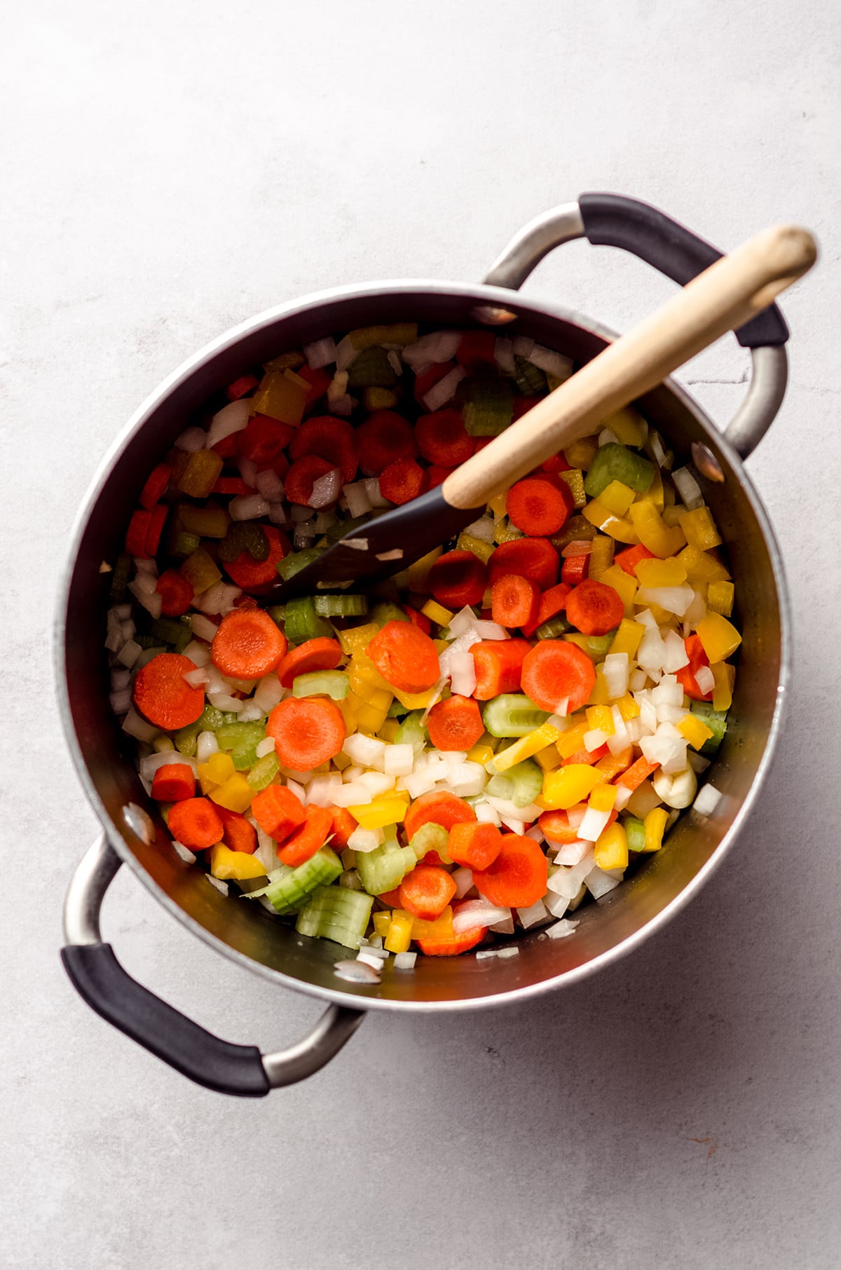 aerial photo of chopped carrots, celery, bell pepper, onion, and garlic in a large pot with a spatula