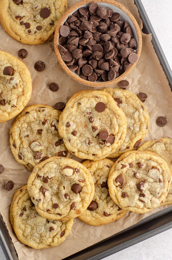 aerial photo of chocolate chip cookies on a baking sheet lined with parchment and a bowl of chocolate chips