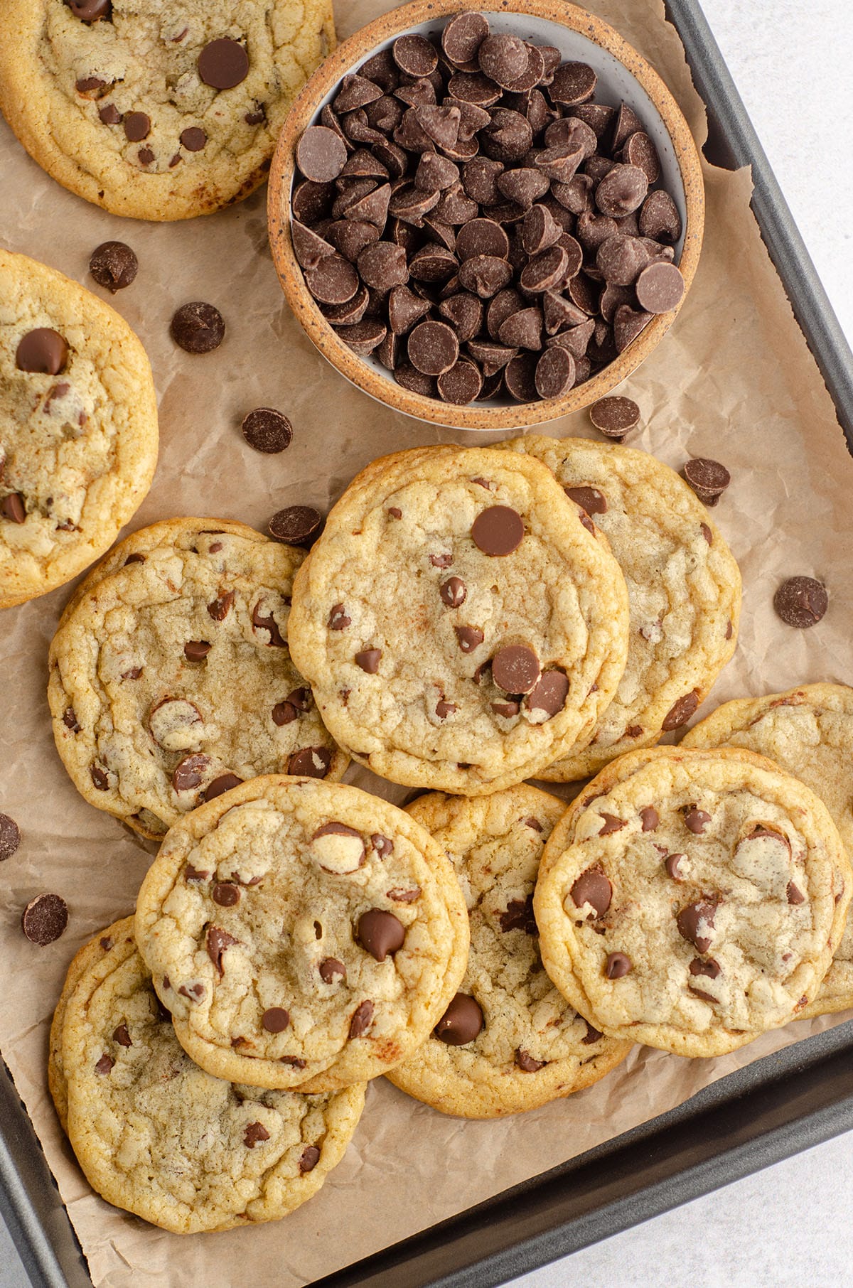 aerial photo of chocolate chip cookies on a baking sheet lined with parchment and a bowl of chocolate chips
