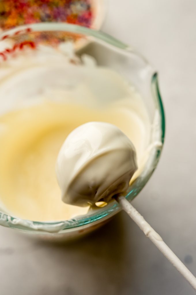 A cake pop getting dipped into coating.