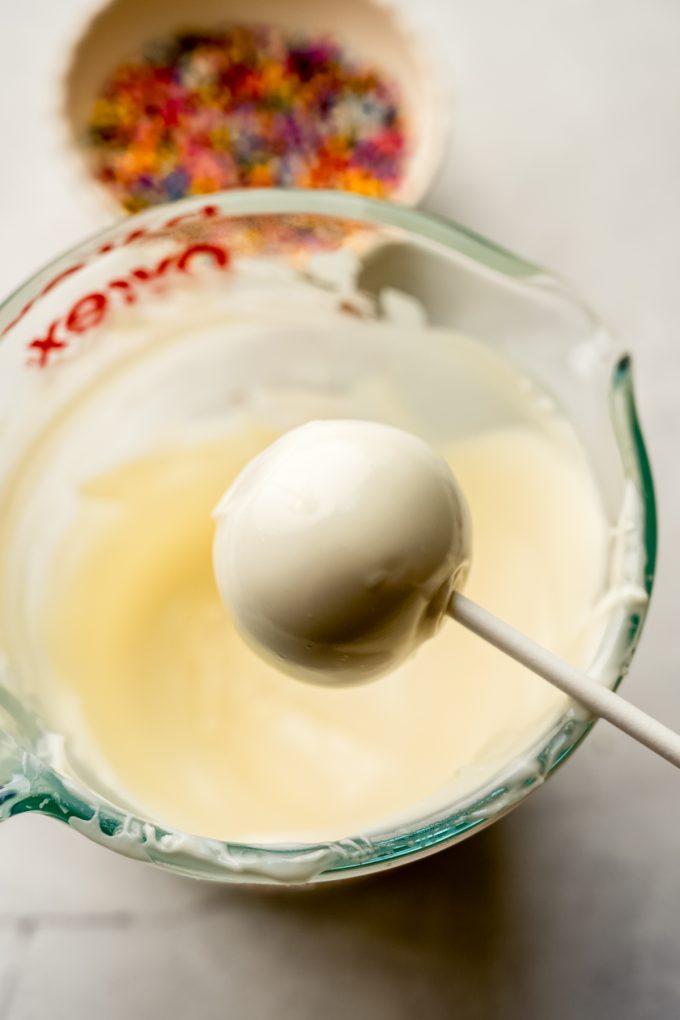 A cake pop getting dipped into coating.