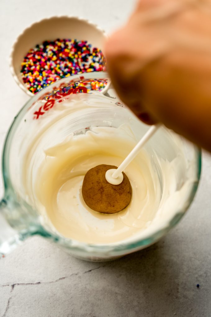 A cake pop getting dipped into coating.
