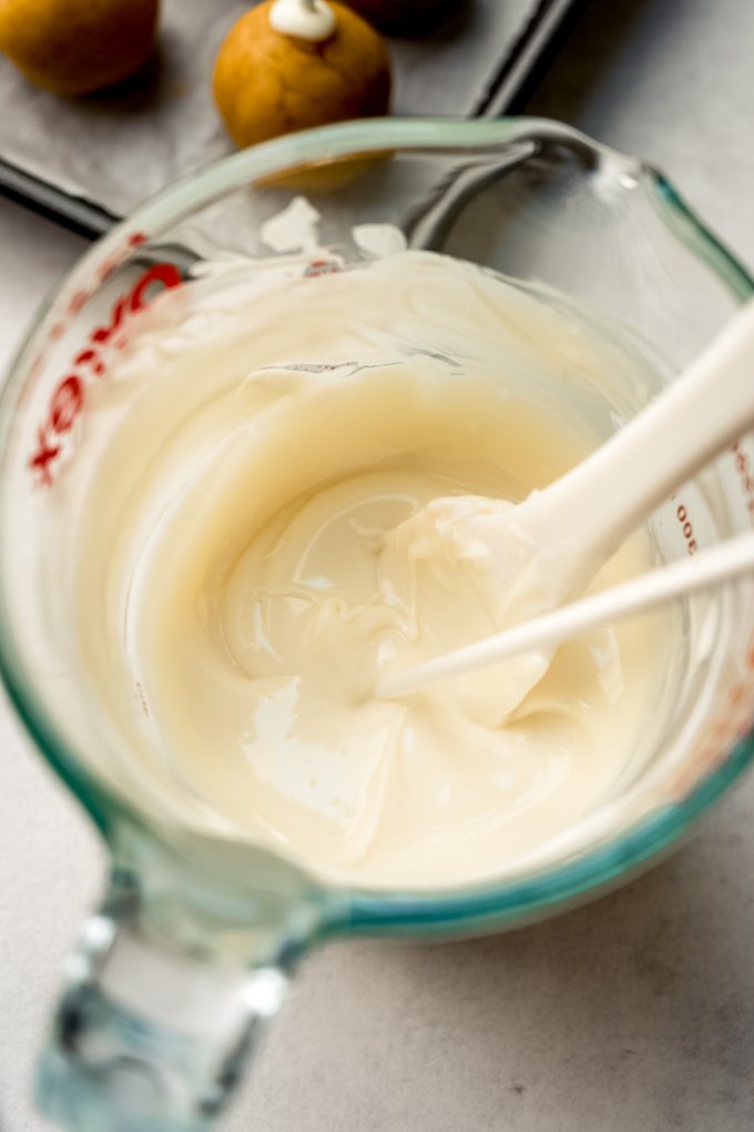 A measuring cup of melted cake pop coating with a stick in it.
