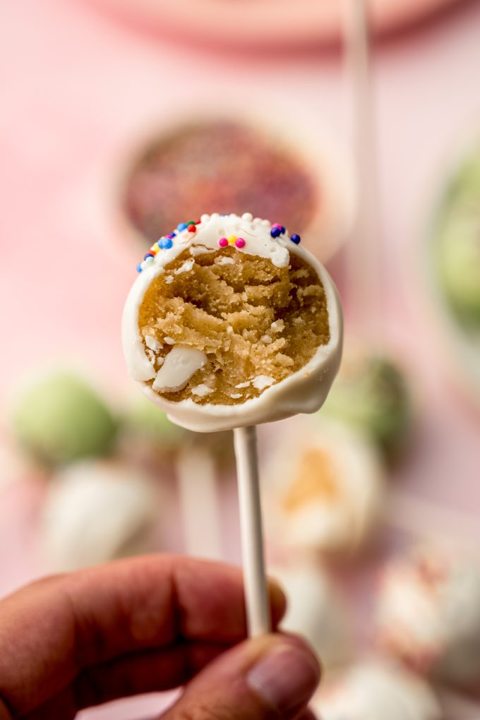 Someone is holding a cake pop with a bite taken out of it.
