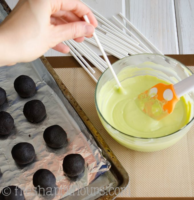dipping a lollipop stick into a bowl of candy melts to make cake pops