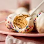 A cake pop with a bite taken out of it on a plate.