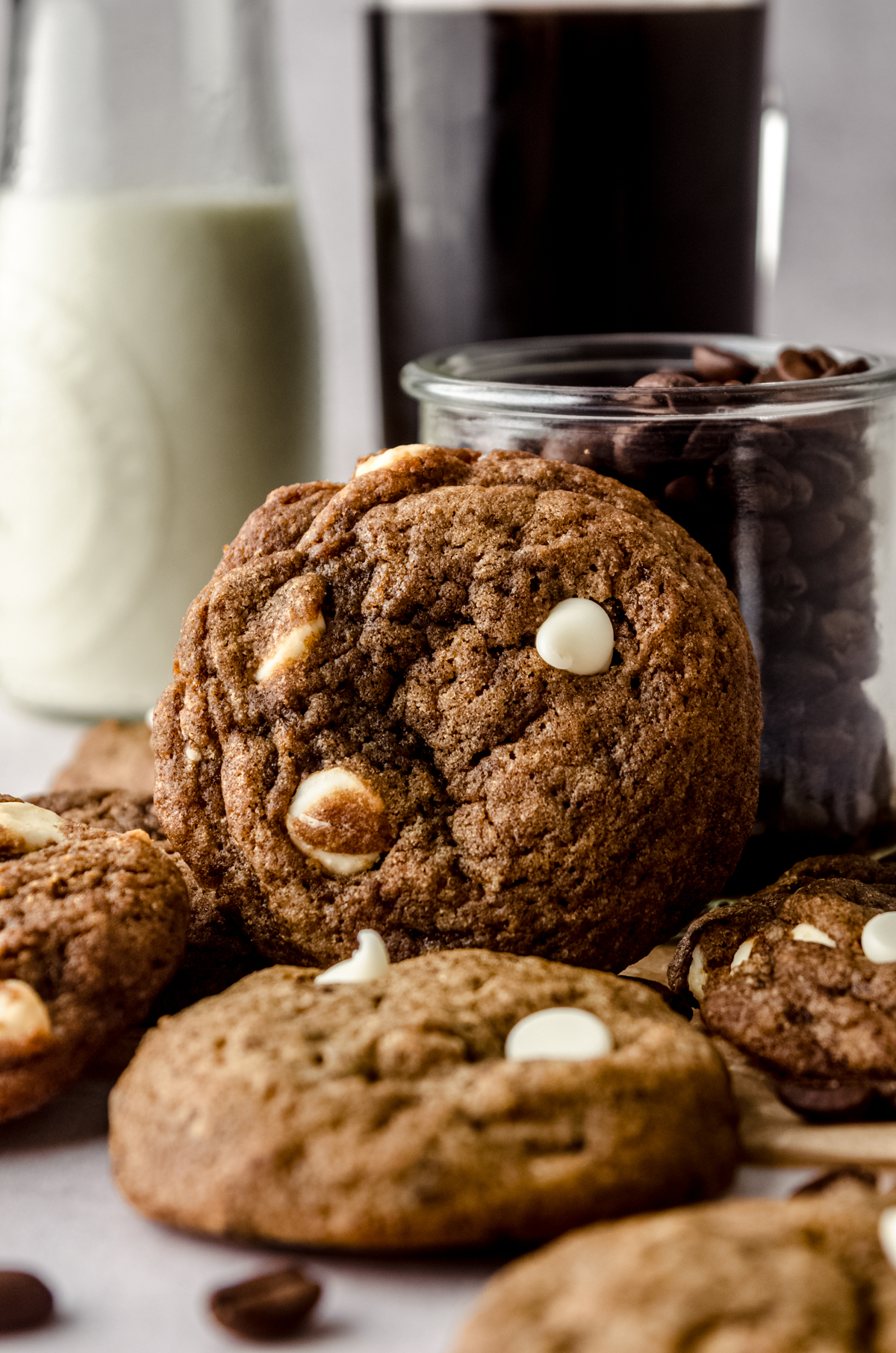 A cappuccino cookies leaning on a jar of coffee beans and milk in the background.