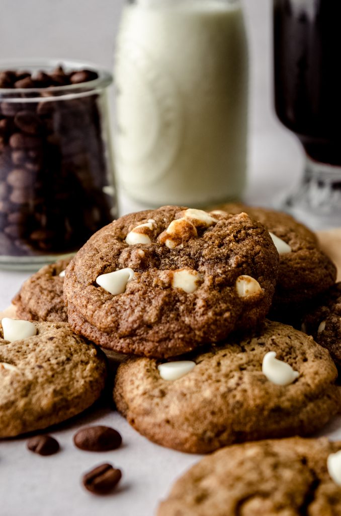 Cappuccino cookies on a surface with coffee, milk, and coffee beans in the background.