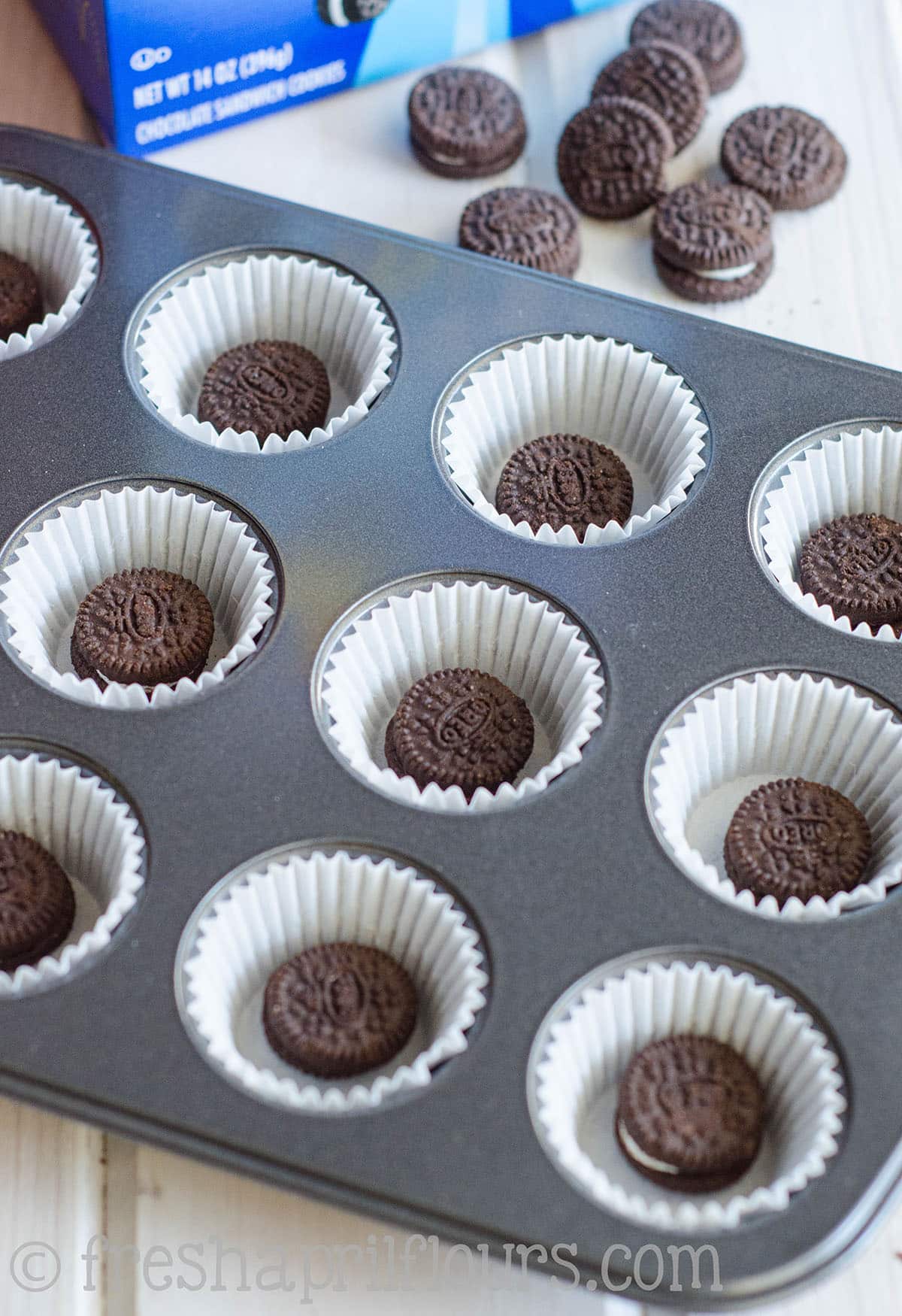 A mini cupcake pan prepped with mini cupcake liners and Oreos in the bottom to make mini cookies and cream cupcakes.