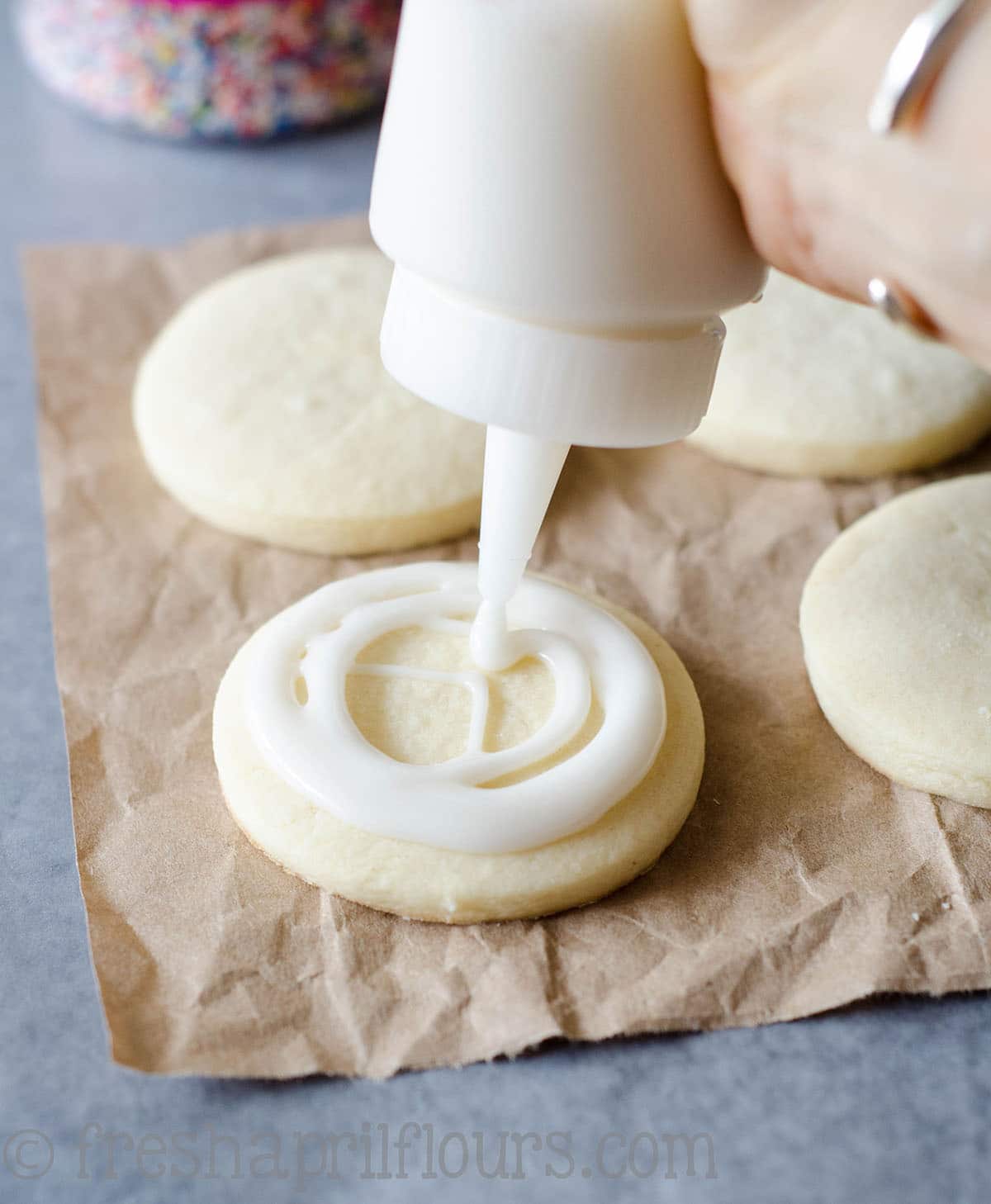 a hand squeezing royal icing onto a cut-out sugar cookie