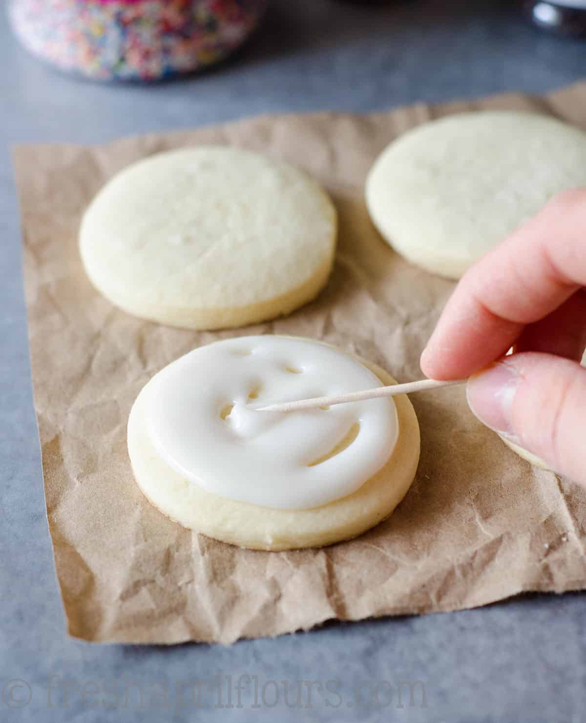 a toothpick spreading royal icing around on a sugar cookie