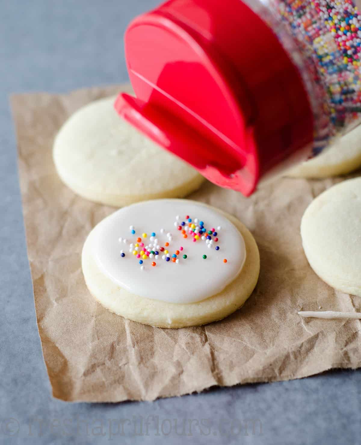 sprinkling non-pareils onto a cut-out sugar cookie with royal icing on it