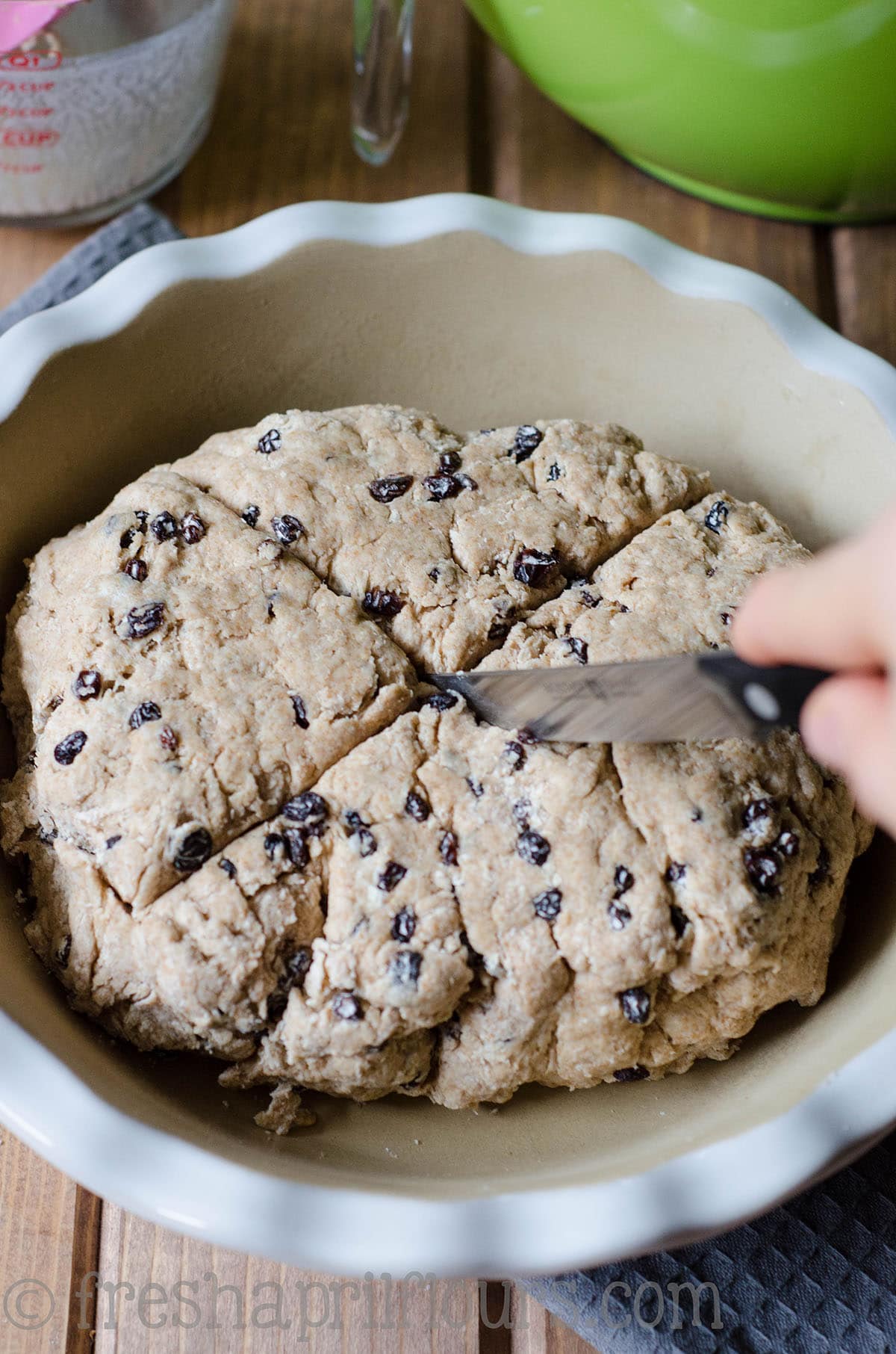 A hand using a knife to slice Irish soda bread before baking.