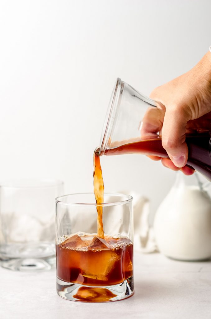 pouring cold brew coffee into a glass with ice
