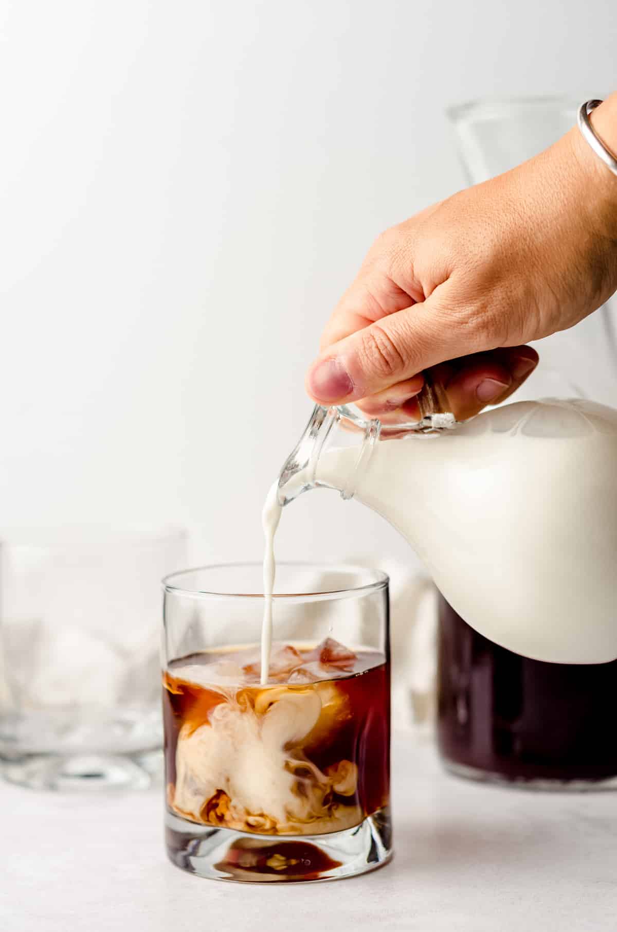 pouring cream into a glass of cold brew coffee