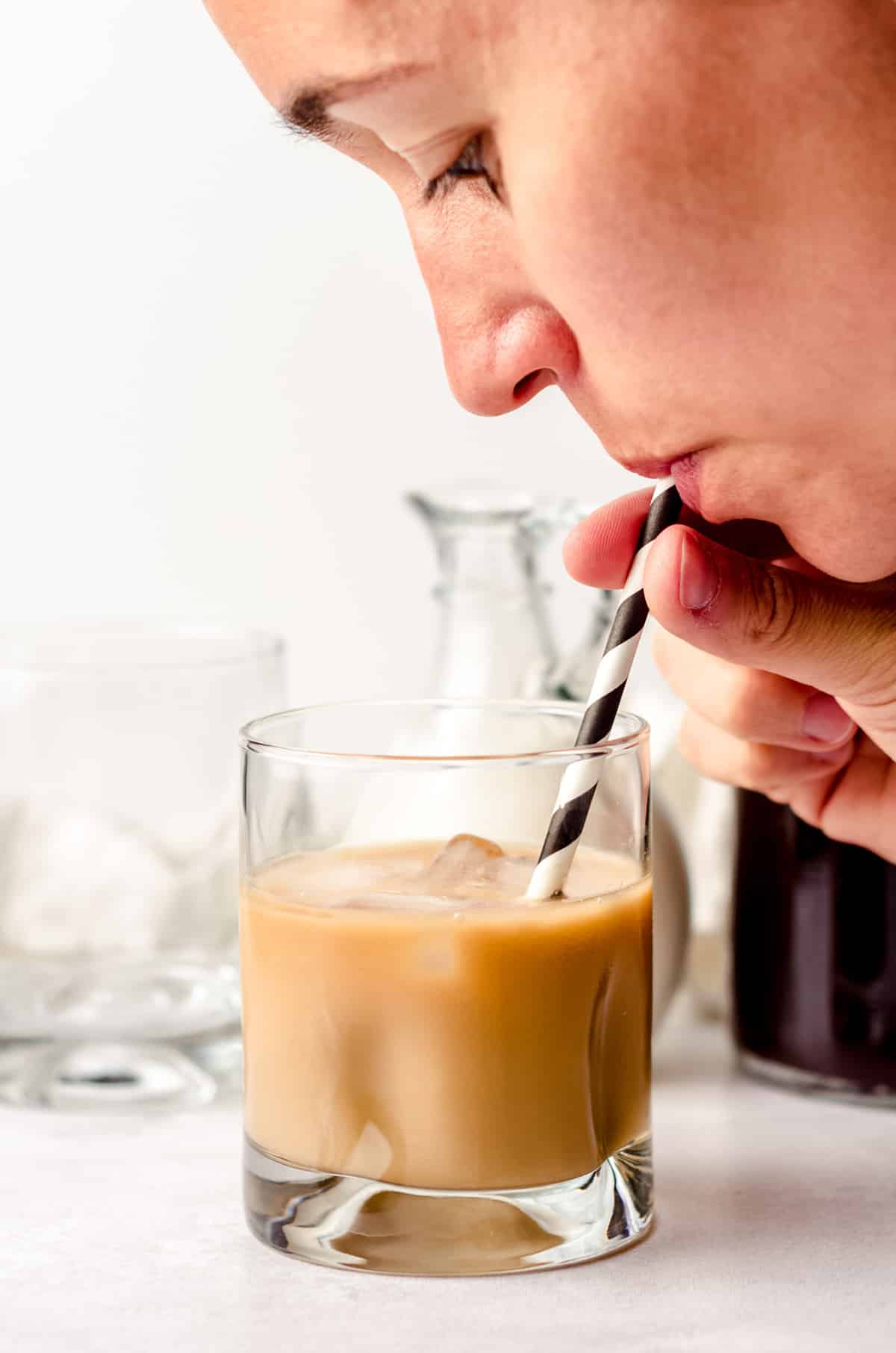 a woman drinking a glass of cold brew coffee from a straw
