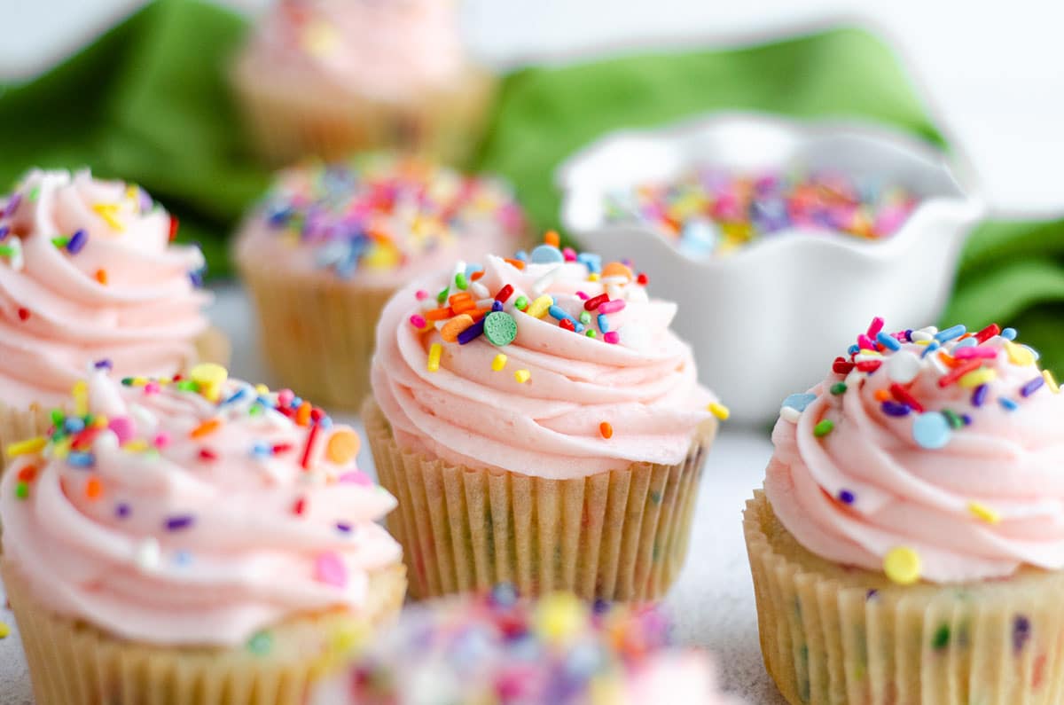 homemade funfetti cupcakes with pink frosting and a bowl of sprinkles in the background