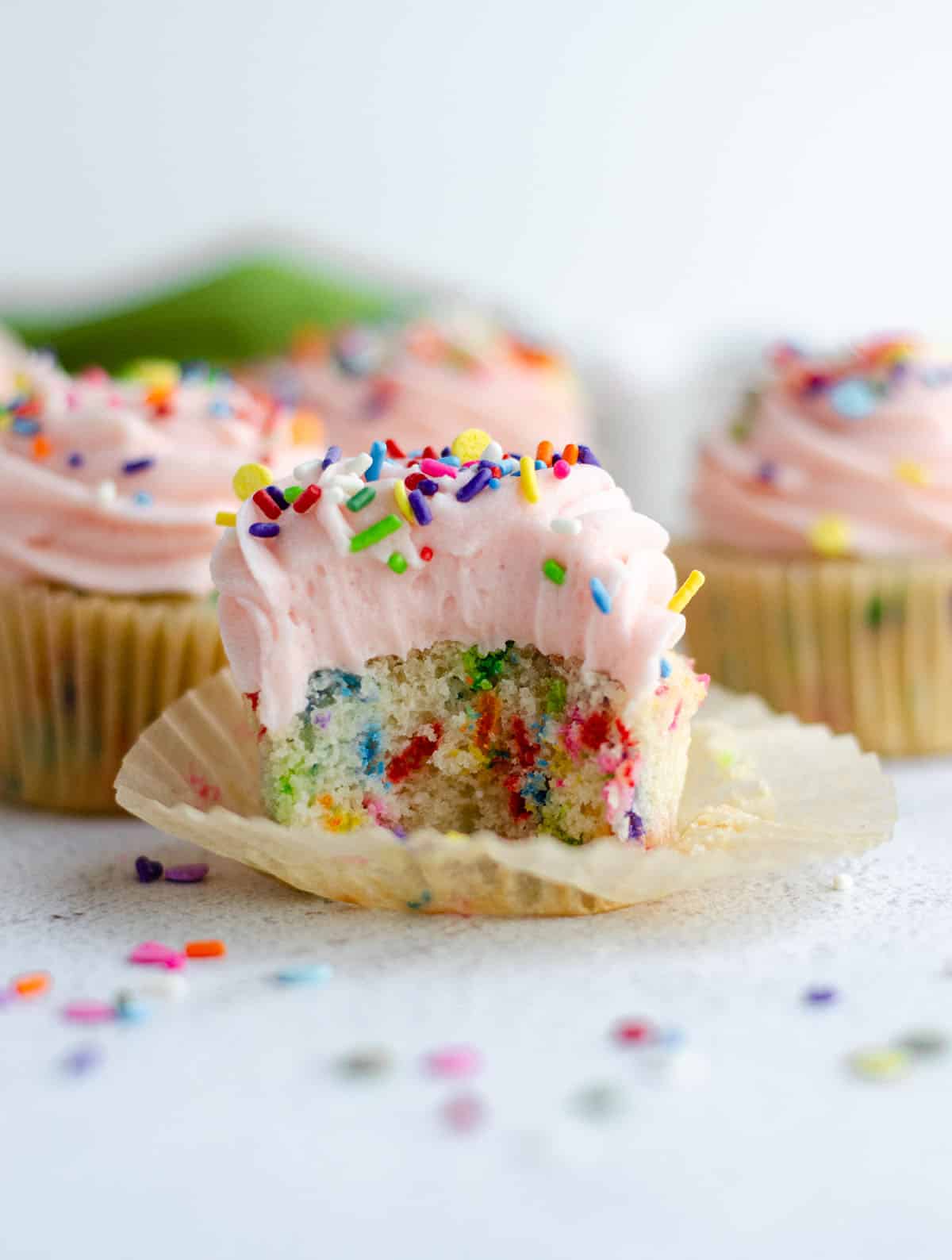 homemade funfetti cupcake with pink frosting and sitting in a wrapper that has been taken off and a bite taken out of it