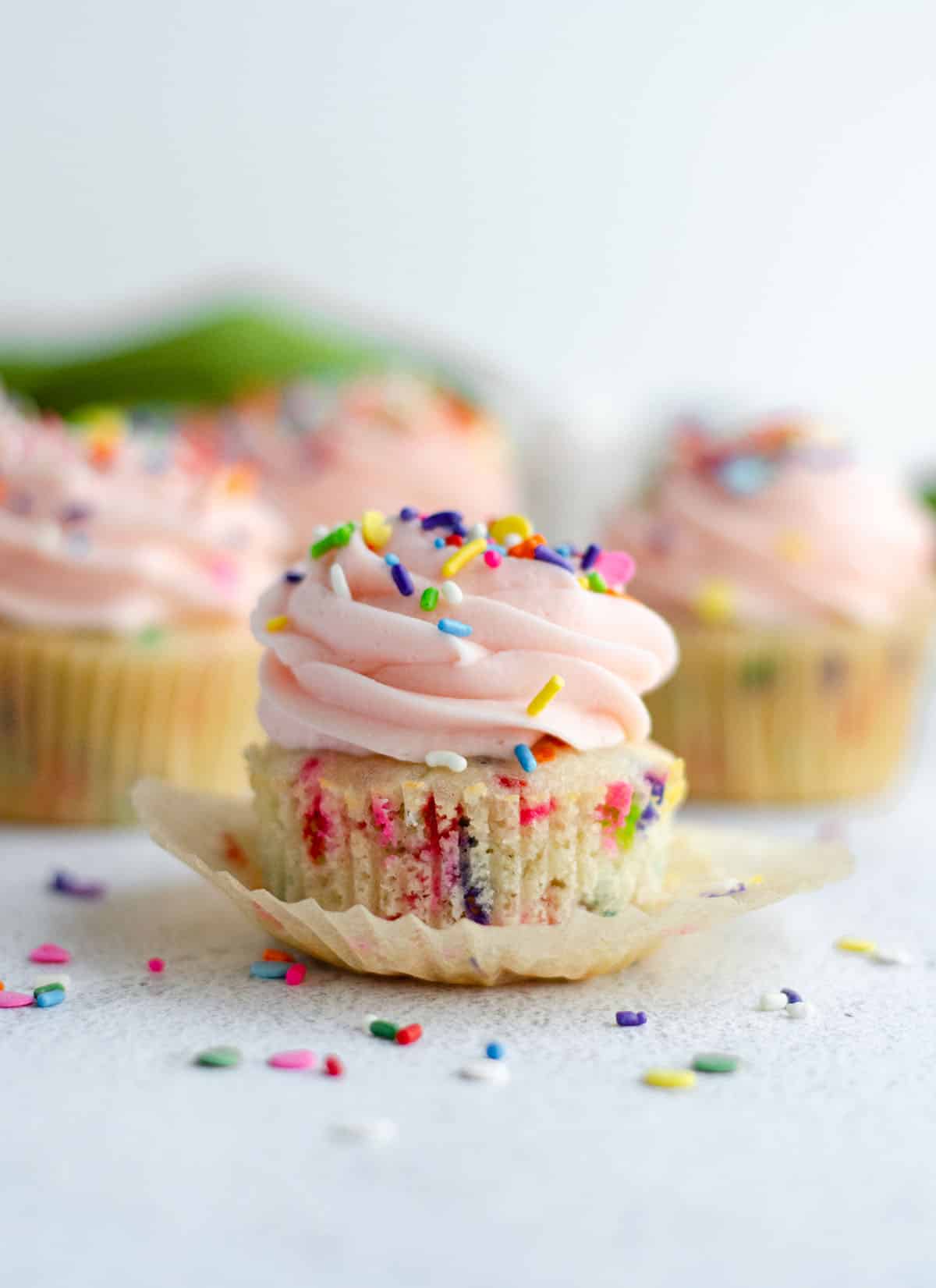 homemade funfetti cupcake with pink frosting and sitting in a wrapper that has been taken off