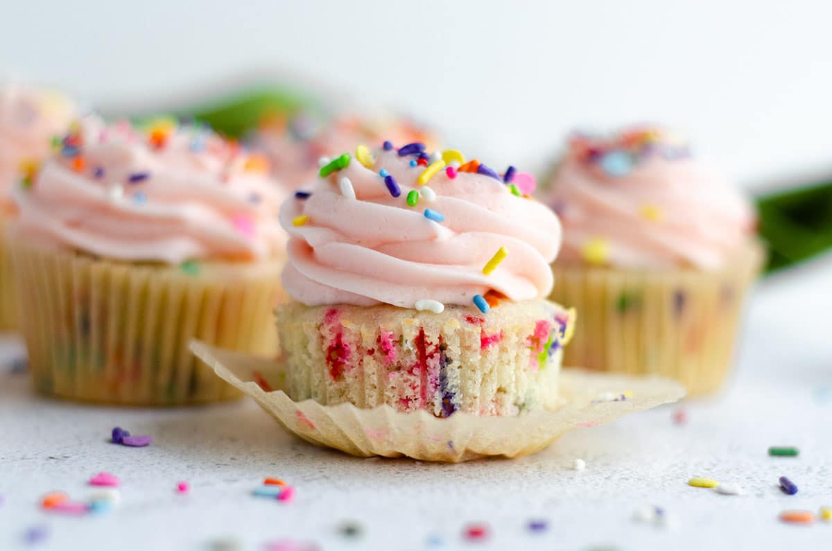 homemade funfetti cupcake with pink frosting and sitting in a wrapper that has been taken off