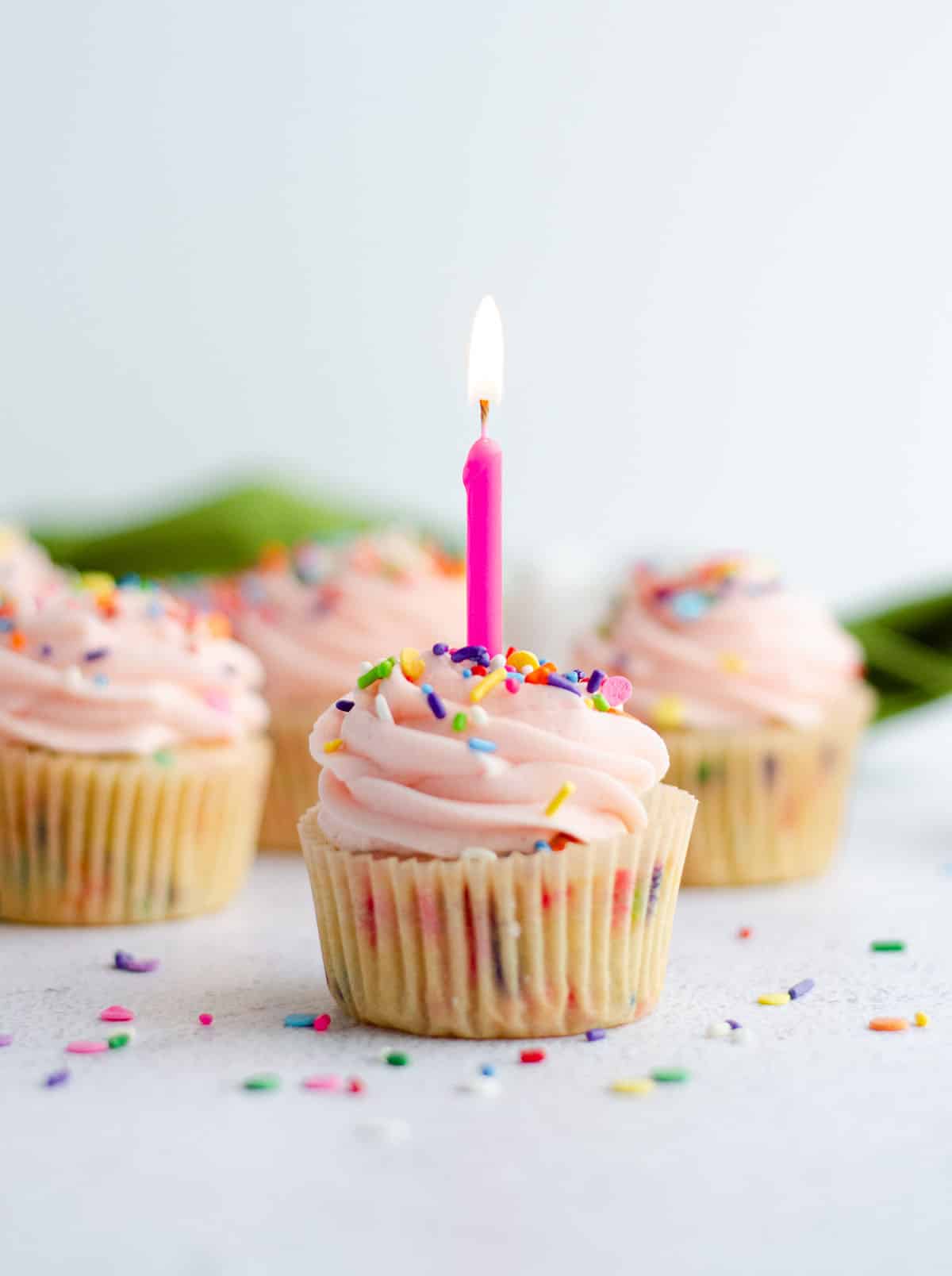 homemade funfetti cupcake with pink frosting and a lighted pink birthday candle 